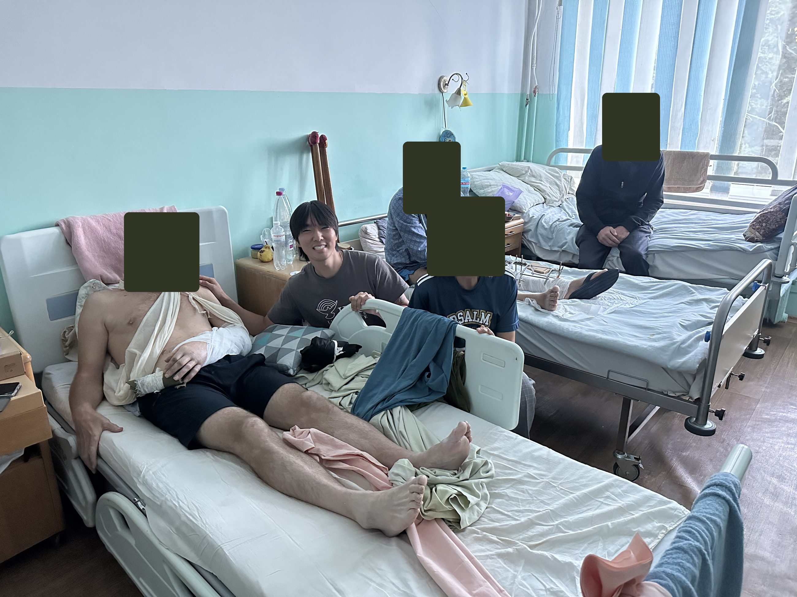 Daniel smiling beside a hospital bed; other faces covered