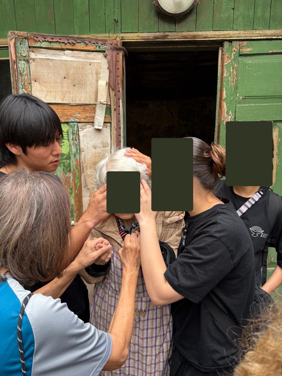 Daniel praying with friends for an older woman; other faces covered